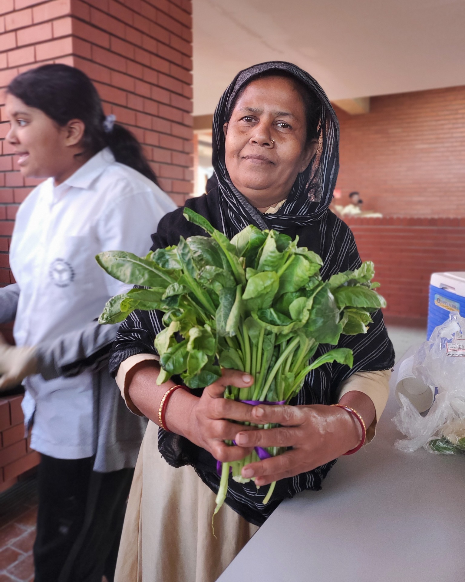 An academic support staff holding vegetables freshly grown by the Grade 7 students. 